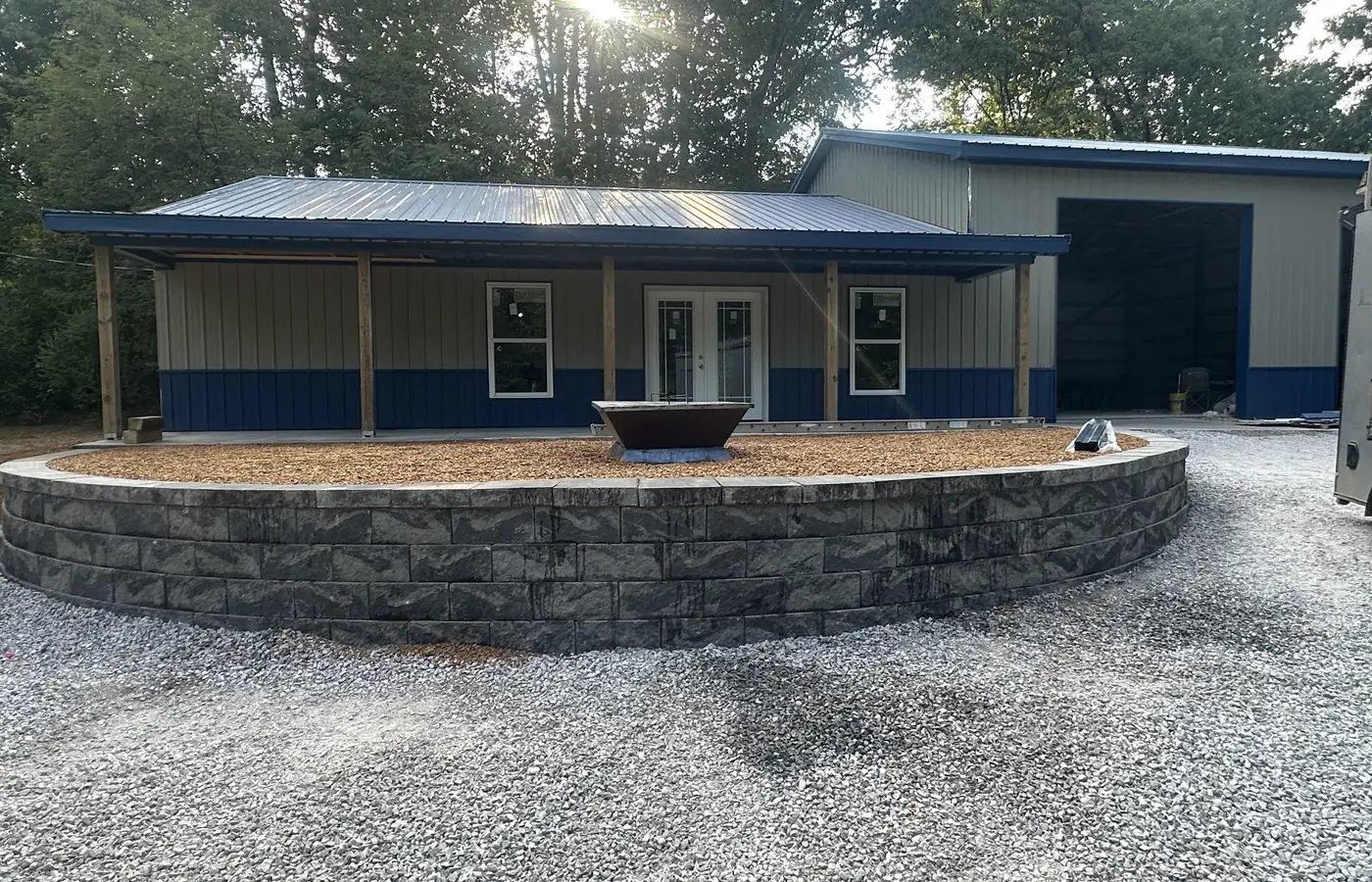 A finished curved retaining wall of charcoal block wrapping a mulched bed in front of a newly built pole barn